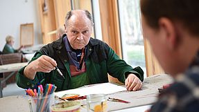 Man paints in the Lobetal creative workshop. He holds a paintbrush in his hand and looks into the camera.