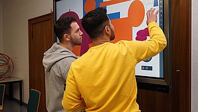 Two students learning on a touchscreen monitor.