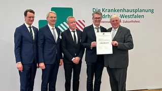 Fünf Männer lächeln und zwei davon halten eine Urkunde.