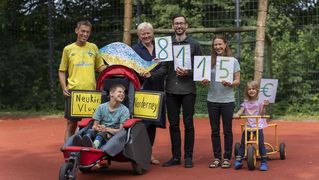 Familie hält mit Bethel-Mitarbeitenden die Spendensumme auf Schildern hoch.