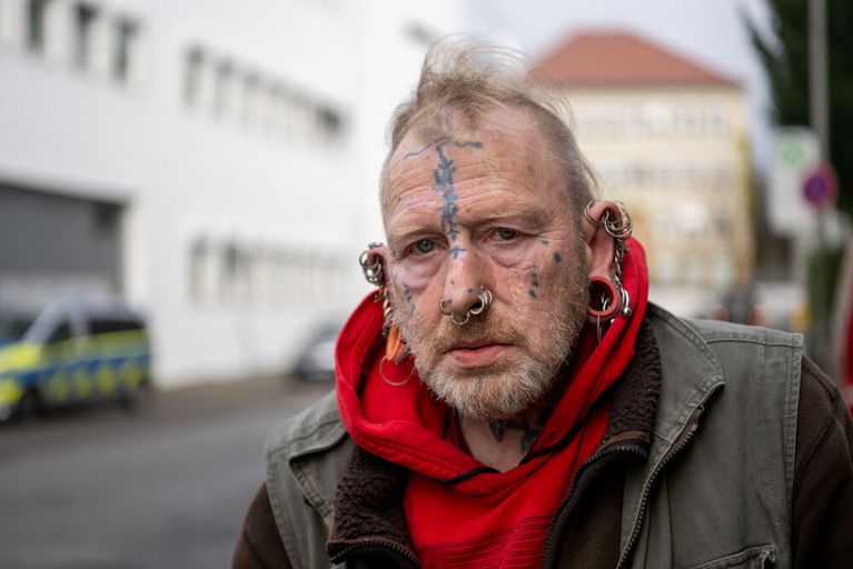 Mann mit vielen Piercings im Gesicht schaut in die Kamera