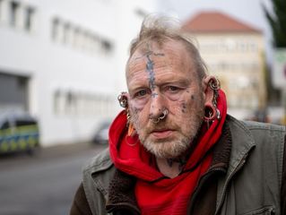 Mann mit vielen Piercings und Tattoos im Gesicht schaut in die Kamera