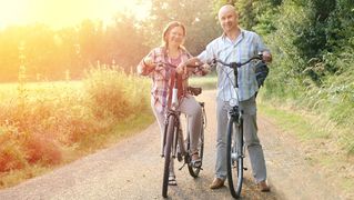 Frau und Mann auf ihren Fahrrädern. Im Hintergrund geht die Sonne unter. 