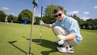 Junge hält vor dem Loch einen Golfball hoch.