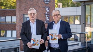 Dr. Rainer Norden und Pastor Ulrich Pohl stehen mit Jahresberichten in den Händen auf der Dachterrasse der Hauptverwaltung. 