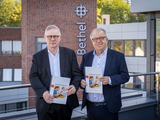 Dr. Rainer Norden und Pastor Ulrich Pohl stehen mit Jahresberichten in den Händen auf der Dachterrasse der Hauptverwaltung.