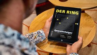 Eine Person sitzt mit einem Tablet mit der digitalen Ausgabe von DER RING am Tisch.