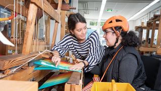 Eine Frau hilft einer anderen frau bei der Bedienung eines Webstuhls.