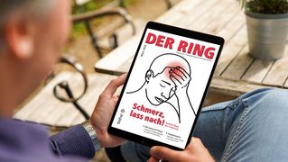 Person sitzt an einem Gartentisch und hält ein Tablet mit der digitalen Ausgabe von DER RING in den Händen.