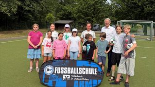 EvKB-Geschäftsführer Dr. Matthias Ernst steht mit Kindern der Fußballschule auf dem Sportplatz.