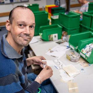 Carsten Hirsch sitzt an seinem Arbeitsplatz und sortiert Briefmarken