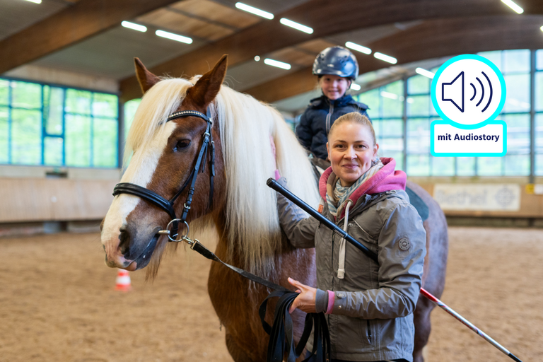 Ein Mädchen sitzt auf einem Pferd. Eine junge Frau steht neben dem Pferd.