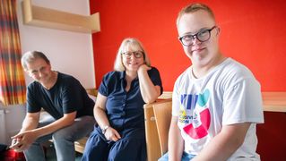 Andreas Karger, Vibeke Wellner und Mika sitzen in einem Zimmer auf dem Bett.