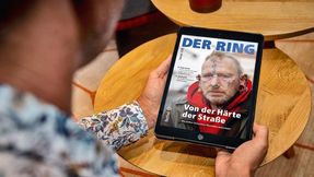 Ein Mann sitzt am Tisch und liest den digitalen RING auf dem Tablet.