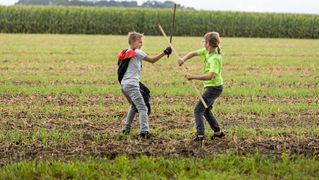 Kai plays with another child on a meadow with sticks.