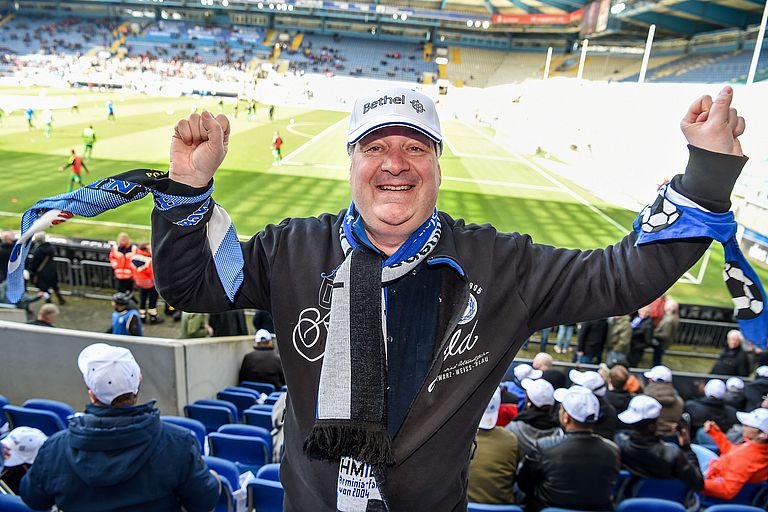 Rainer Wollenburg steht auf der Tribühne im Fußball-Stadion und hält jubelnd beide Arme in die Höhe.