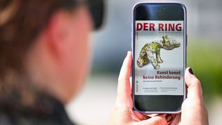 Eine Person mit Sonnenbrille hält ein Smartphone mit der digitalen Juni-Ausgabe von DER RING in den Händen