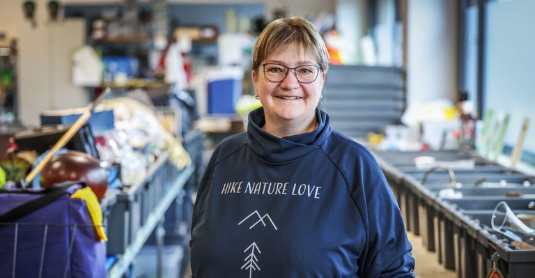 Heike Szillmischkies lächelt in die Kamera. Hinter ihr sind viele Boxen mit Klamotten.