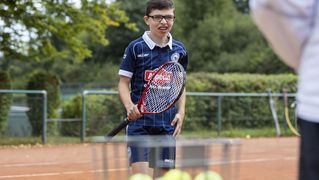 Ein Junge schaut seinen Trainer an. In der Hand hält er einen Tennisschläger.