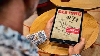 Ein Mann sitzt am Tisch und liest den digitalen RING auf dem Tablet.