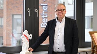 Pastor Pohl steht am Fenster in seinem Büro. Auf der Fensterbank steht eine Figur des Leinewebers.