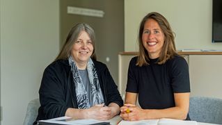 Silke Benter und Katrin Klaphake sitzen an einem Tisch und lächeln in die Kamera