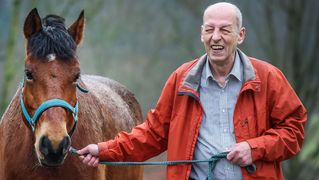 Ein älterer Mann (rechts) führt ein Pferd (links) an einer Leine.