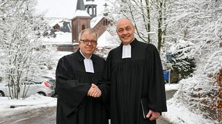 Pastor Ulrich Pohl und Pastor Bartolt Haase schütteln sich die Hände vor der verschneiten Zionskirche.